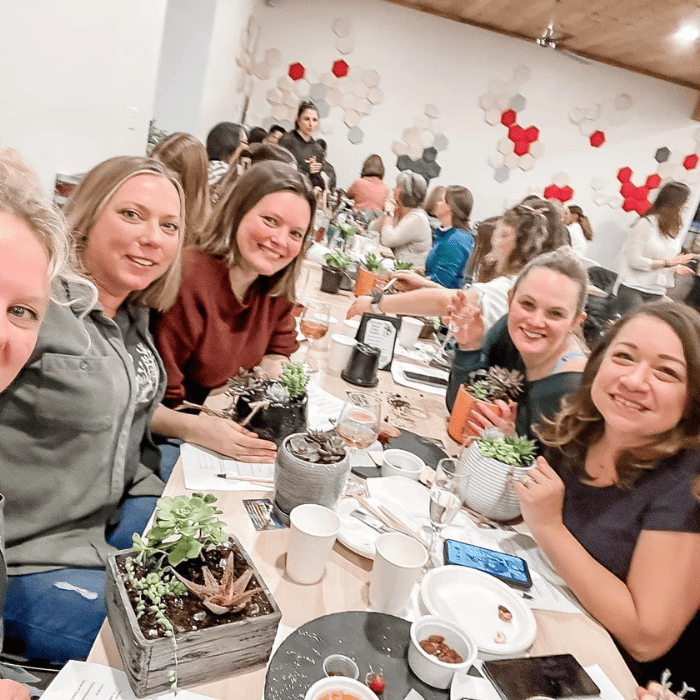 women smiling seated around a table at a plant and sip party