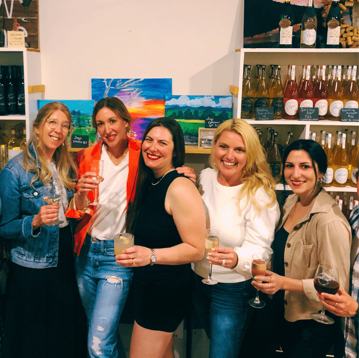 five women having fun posing for the camera with wine