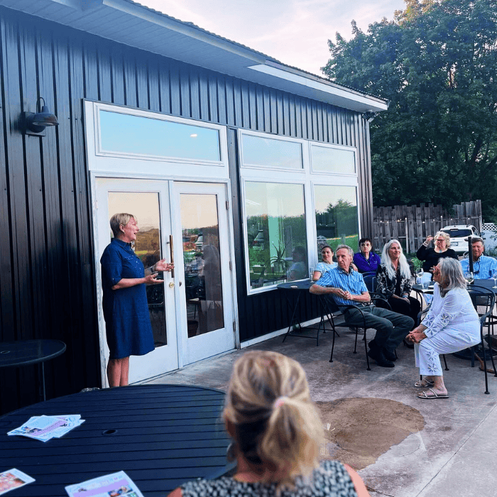 a woman giving a speech to guest on the tasting room patio