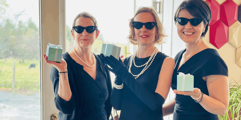 Three women in little black dresser with pearls and sunglasses on and their Tiffany ring box gift